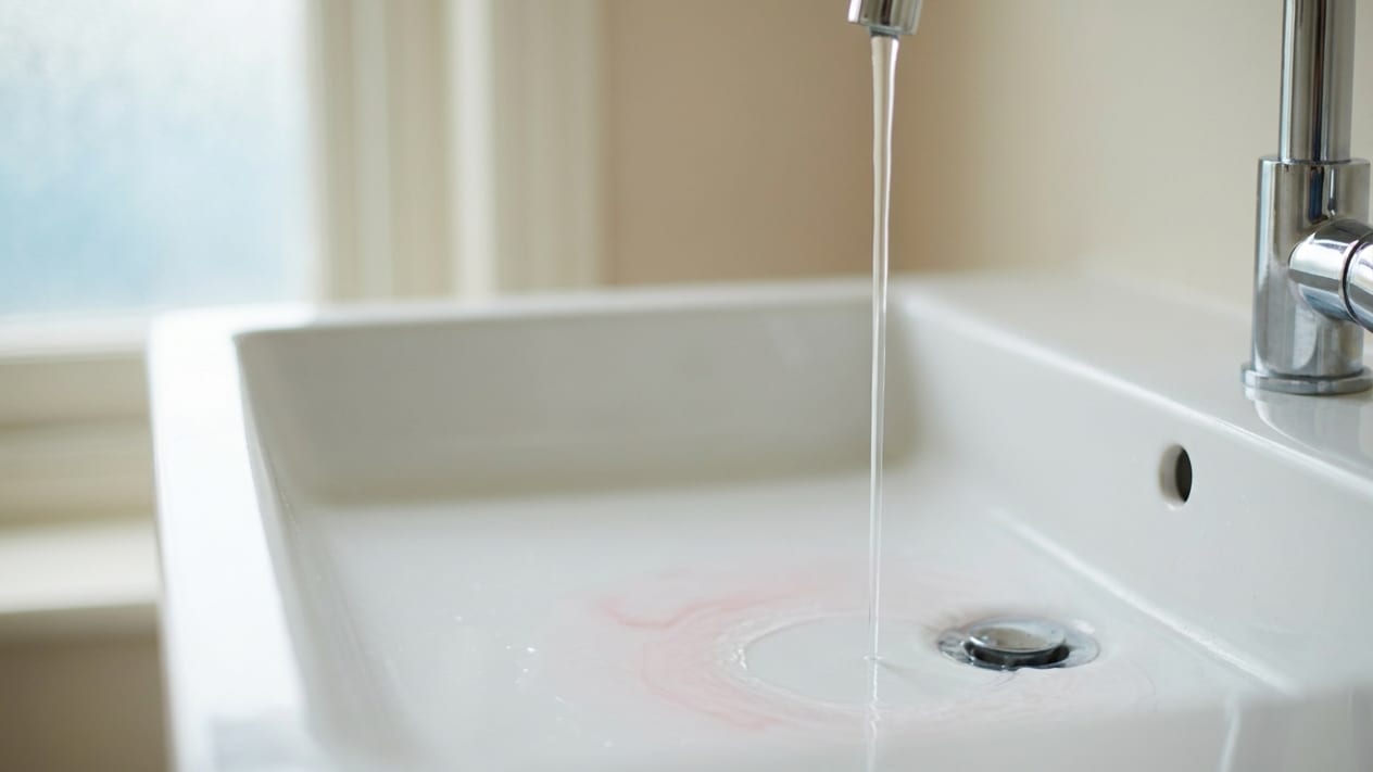 A white bathroom basin after brushing, with a faint trace of pink in the water.